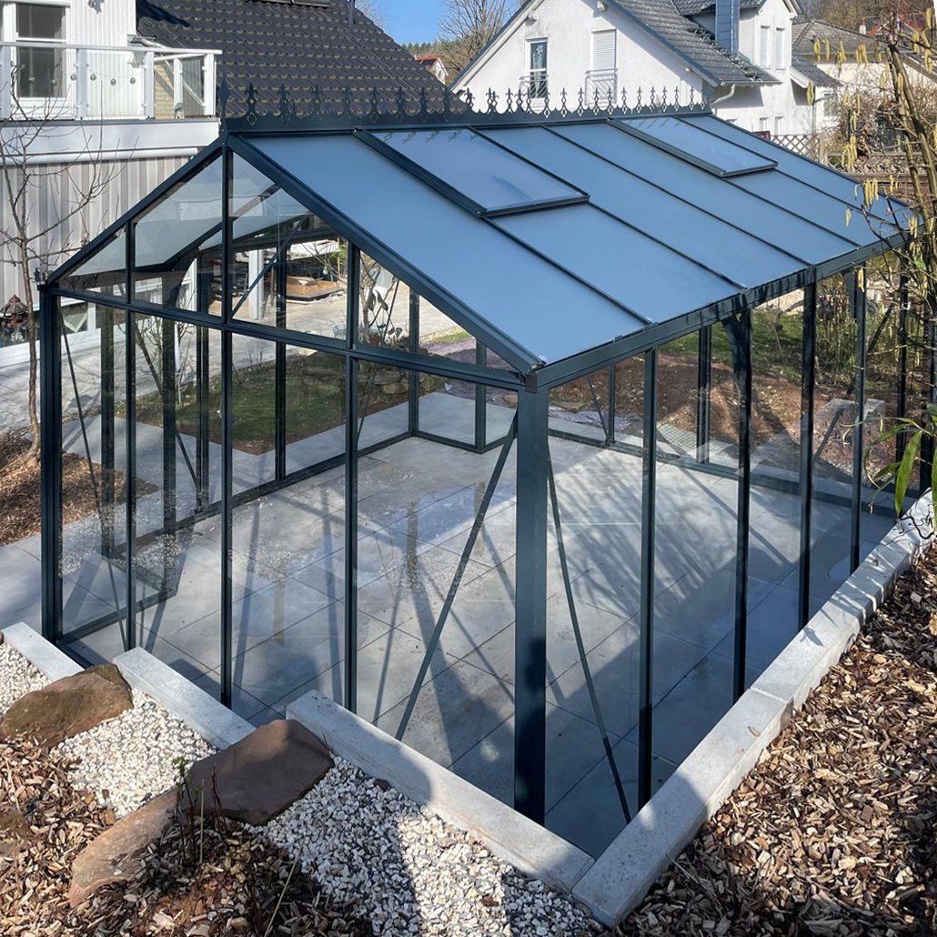 T-formet orangeri i glas og aluminium placeret på et forberedt fundament