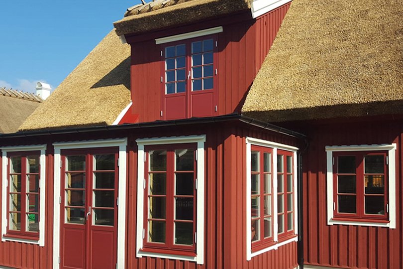 rødt to-etagers hus med stråtækt tag og matchende vinduer og døre